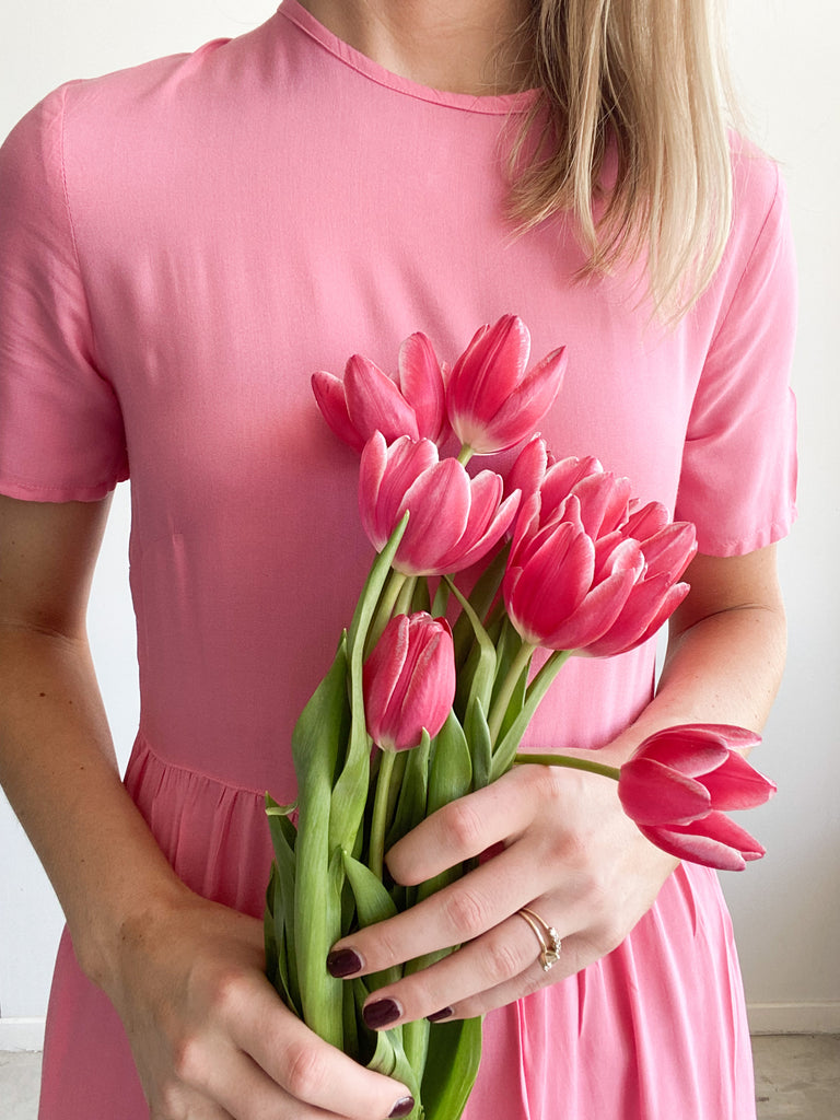 Woman wearing a barbie Zozi Dress facing forwards and holding flowers
